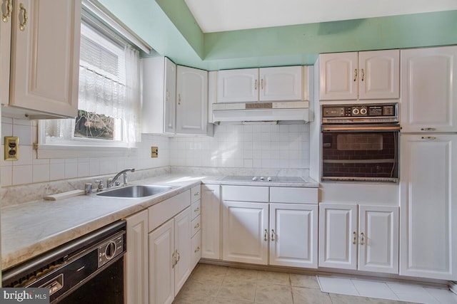 kitchen featuring under cabinet range hood, a sink, light countertops, decorative backsplash, and black appliances