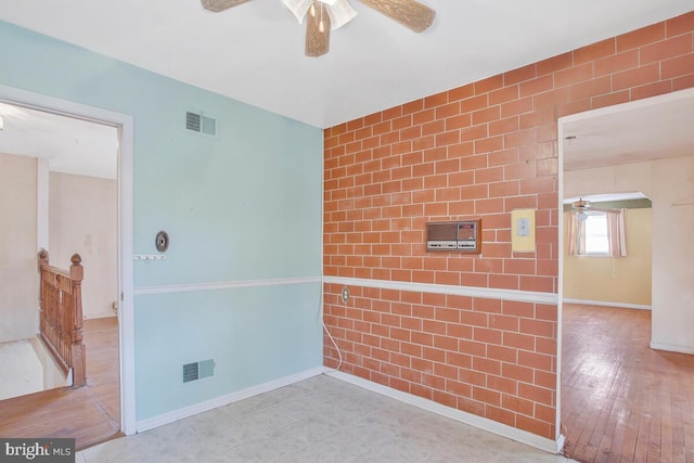 empty room with visible vents, an accent wall, ceiling fan, baseboards, and hardwood / wood-style flooring