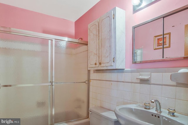 bathroom with toilet, enclosed tub / shower combo, tile walls, and a sink