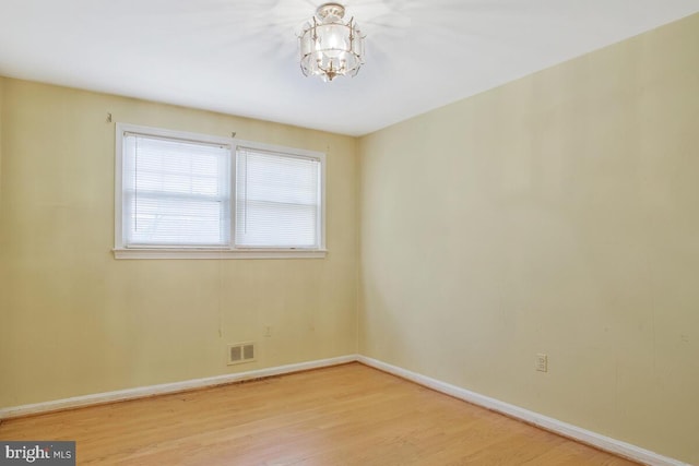 spare room featuring light wood finished floors, an inviting chandelier, visible vents, and baseboards