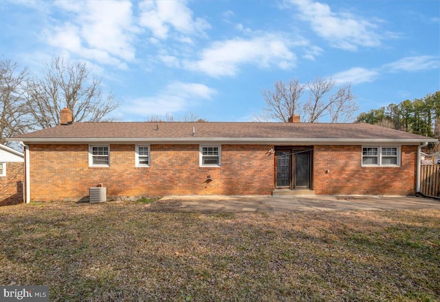 rear view of property featuring brick siding, a chimney, cooling unit, and a lawn