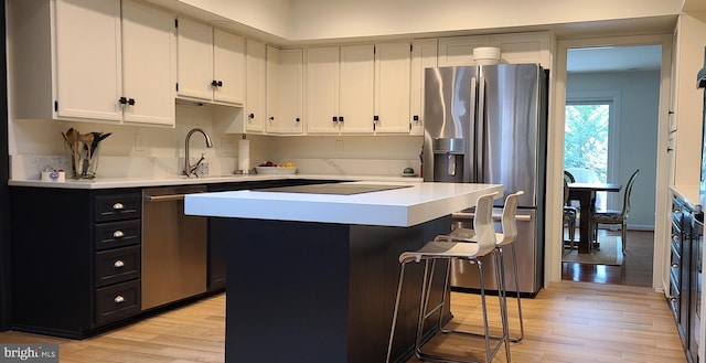 kitchen with dark cabinets, stainless steel appliances, a kitchen breakfast bar, light countertops, and light wood finished floors