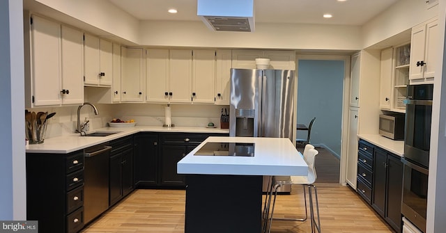 kitchen featuring light countertops, appliances with stainless steel finishes, a sink, a kitchen island, and dark cabinets