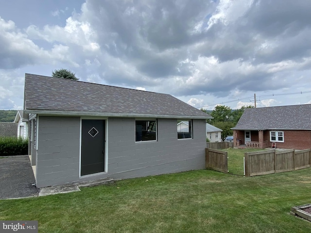 rear view of house with a shingled roof, concrete block siding, a yard, and fence