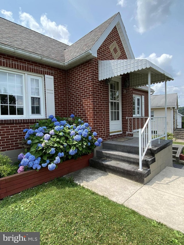 view of exterior entry featuring brick siding, roof with shingles, and a porch