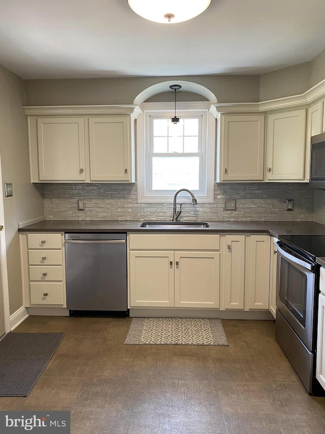 kitchen featuring stainless steel appliances, dark countertops, a sink, and backsplash