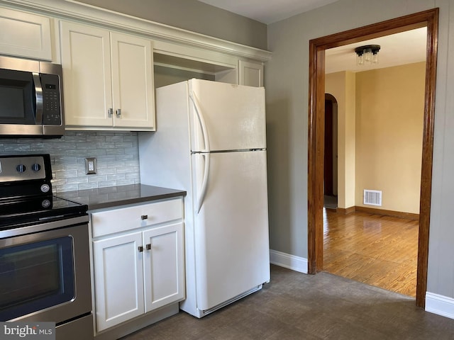 kitchen featuring arched walkways, stainless steel appliances, visible vents, backsplash, and dark countertops