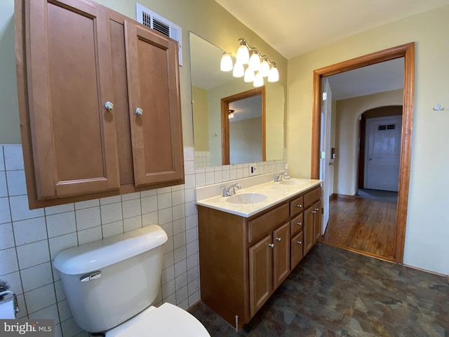 full bathroom featuring double vanity, a sink, toilet, and tile walls