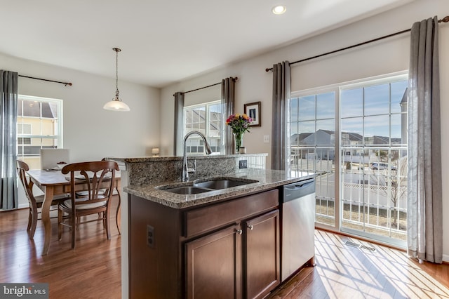 kitchen featuring dark wood-type flooring, dark stone counters, a sink, dishwasher, and pendant lighting