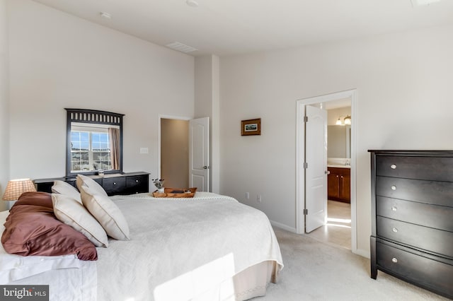 bedroom with light carpet, ensuite bathroom, a towering ceiling, and baseboards