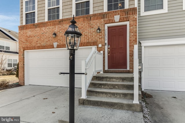 view of exterior entry featuring a garage, driveway, and brick siding