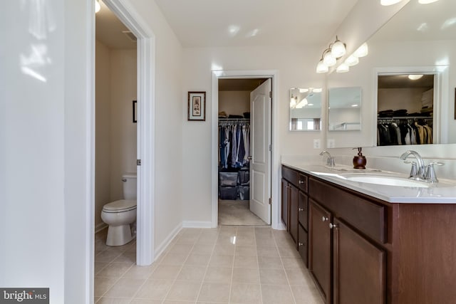 full bath featuring double vanity, toilet, tile patterned floors, a walk in closet, and a sink