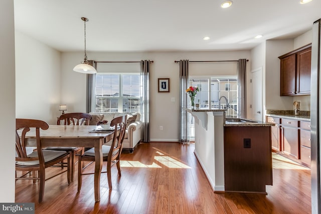 kitchen featuring recessed lighting, stone countertops, an island with sink, wood finished floors, and baseboards