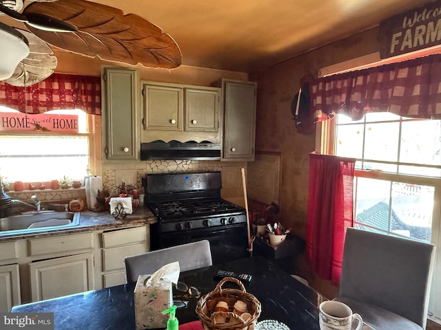 kitchen featuring dark countertops, backsplash, black gas range, a sink, and under cabinet range hood