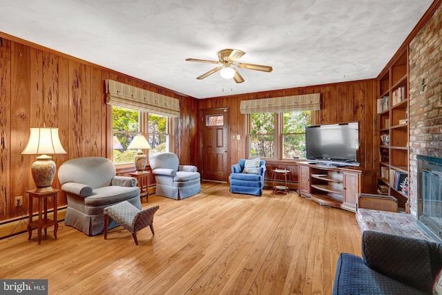 living room with a brick fireplace, built in shelves, light wood-style flooring, and wood walls