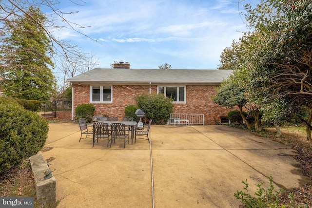 rear view of house featuring brick siding, a chimney, and a patio area