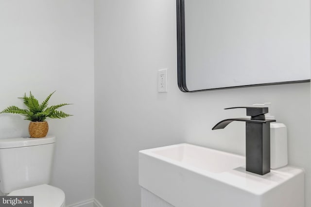 half bath featuring baseboards, toilet, and vanity