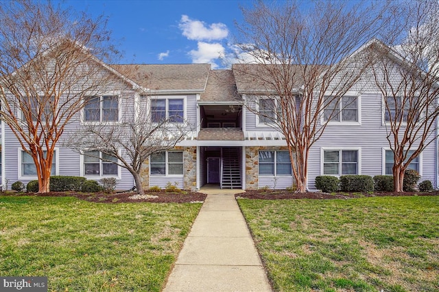 multi unit property with stone siding, a shingled roof, and a front lawn