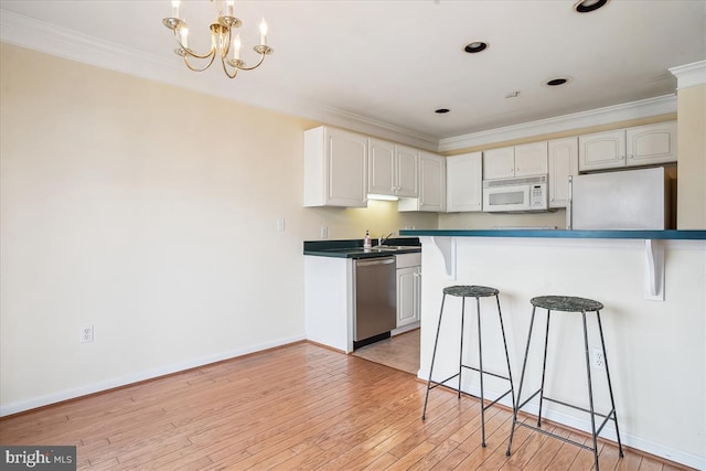 kitchen with light wood-style flooring, a notable chandelier, white appliances, ornamental molding, and a kitchen bar