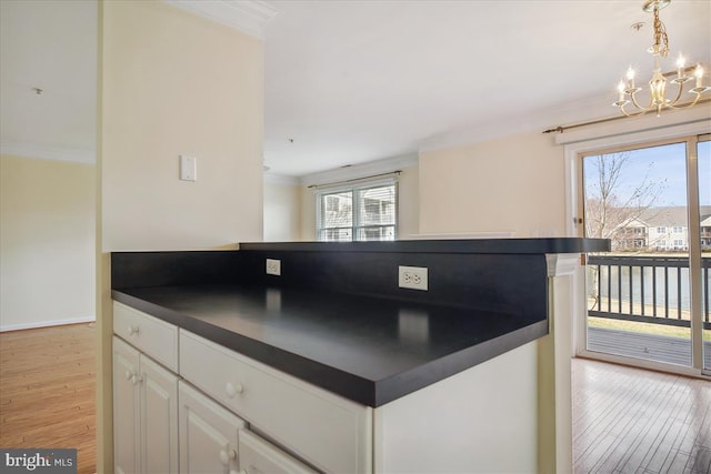 kitchen featuring dark countertops, light wood-style flooring, an inviting chandelier, ornamental molding, and white cabinets