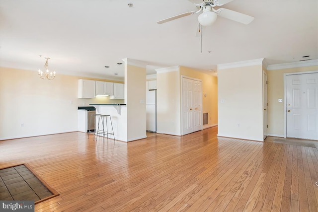 unfurnished living room with ceiling fan with notable chandelier, visible vents, baseboards, light wood-style floors, and ornamental molding