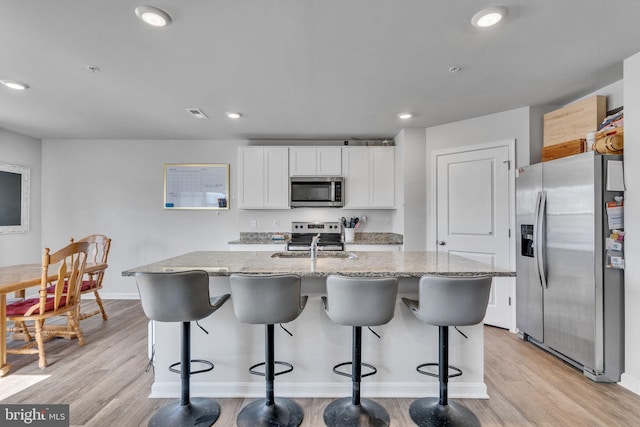 kitchen with a kitchen island with sink, light wood-style flooring, light stone counters, white cabinetry, and stainless steel appliances