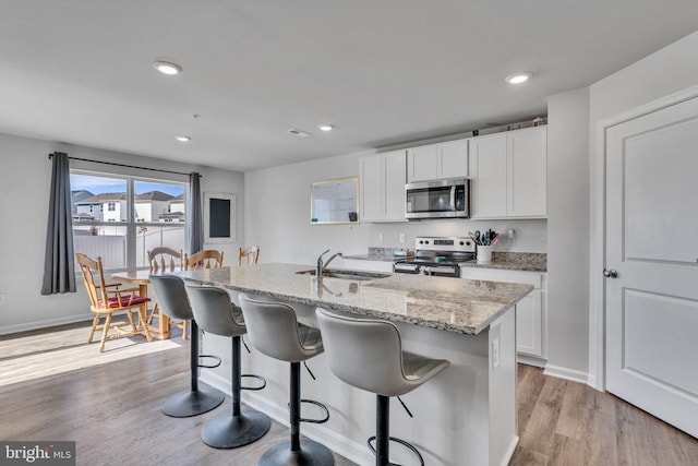 kitchen with a breakfast bar, a sink, stainless steel appliances, white cabinets, and light wood finished floors