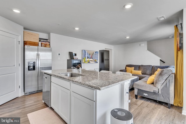 kitchen with an island with sink, light wood-style flooring, appliances with stainless steel finishes, white cabinets, and a sink