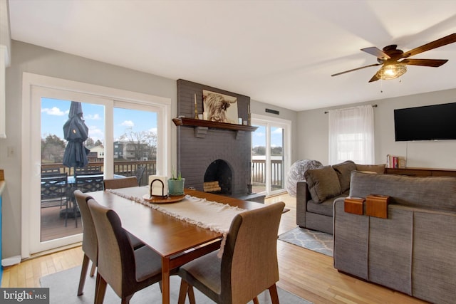 dining room with visible vents, a brick fireplace, a ceiling fan, and light wood finished floors