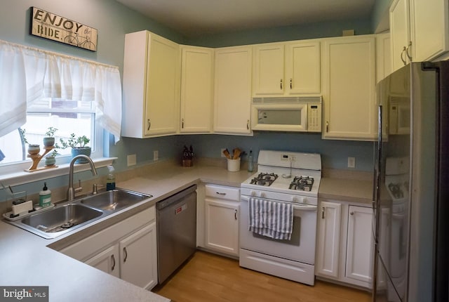 kitchen with white cabinets, white appliances, light countertops, and a sink