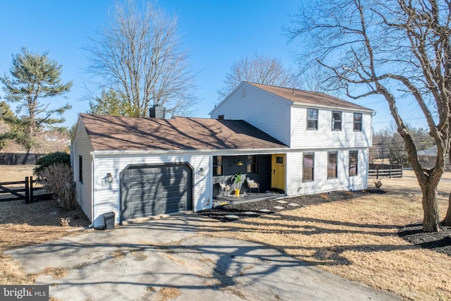 colonial home featuring an attached garage, covered porch, fence, and aphalt driveway