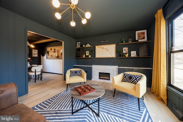 living room featuring a warm lit fireplace, wood finished floors, plenty of natural light, and an inviting chandelier