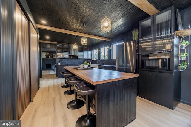 kitchen with light wood-type flooring, a kitchen island, wooden counters, and freestanding refrigerator