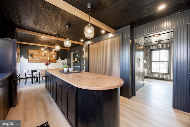 kitchen featuring a kitchen island, dark cabinets, beamed ceiling, freestanding refrigerator, and light wood-style floors