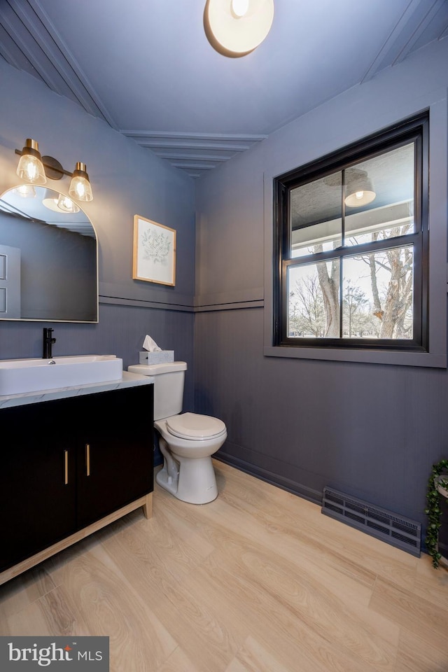 half bathroom featuring toilet, visible vents, wood finished floors, and vanity