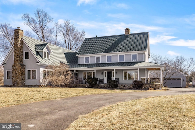 view of front facade with a chimney, metal roof, a standing seam roof, a porch, and a front yard