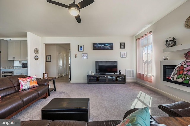 carpeted living area featuring a ceiling fan, a glass covered fireplace, visible vents, and baseboards