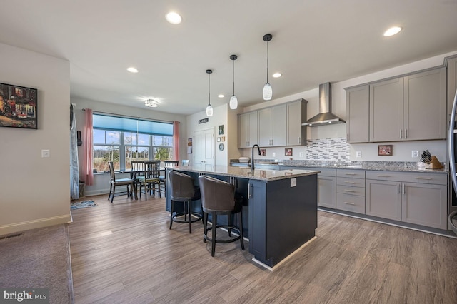 kitchen featuring visible vents, wood finished floors, gray cabinets, wall chimney range hood, and a sink