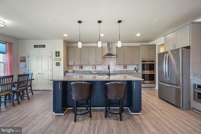 kitchen featuring appliances with stainless steel finishes, gray cabinets, wall chimney range hood, and a center island with sink