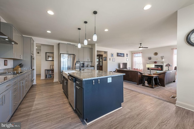 kitchen featuring a glass covered fireplace, appliances with stainless steel finishes, light stone counters, gray cabinetry, and light wood-style floors