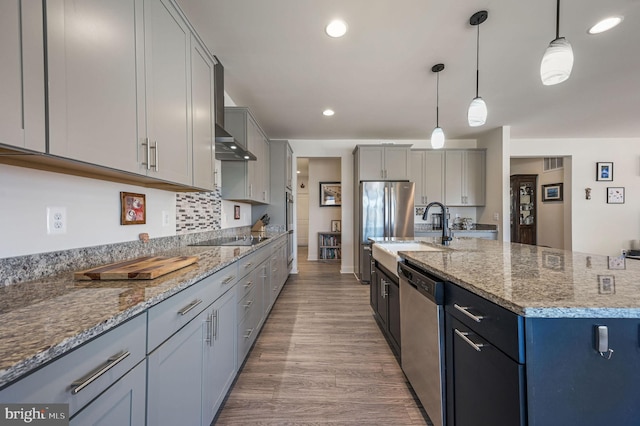 kitchen with light stone counters, pendant lighting, stainless steel appliances, light wood-style floors, and a sink