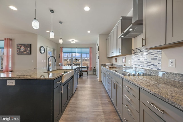 kitchen featuring light wood-style floors, a sink, wall chimney range hood, an island with sink, and black electric cooktop