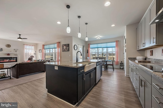 kitchen with wall chimney exhaust hood, black electric stovetop, a sink, and light wood-style flooring