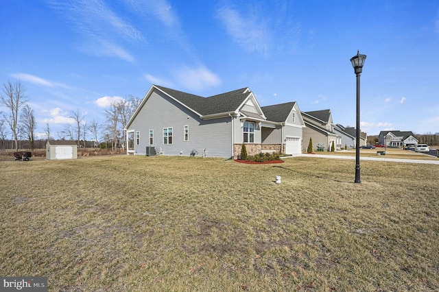 view of side of home featuring roof with shingles, a lawn, central AC unit, a garage, and stone siding