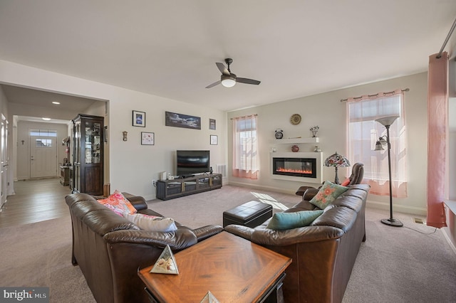 living room featuring a ceiling fan, a wealth of natural light, a glass covered fireplace, and visible vents