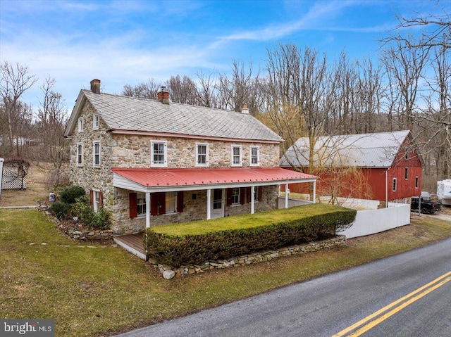 view of front of property featuring stone siding, a porch, a chimney, and a front yard