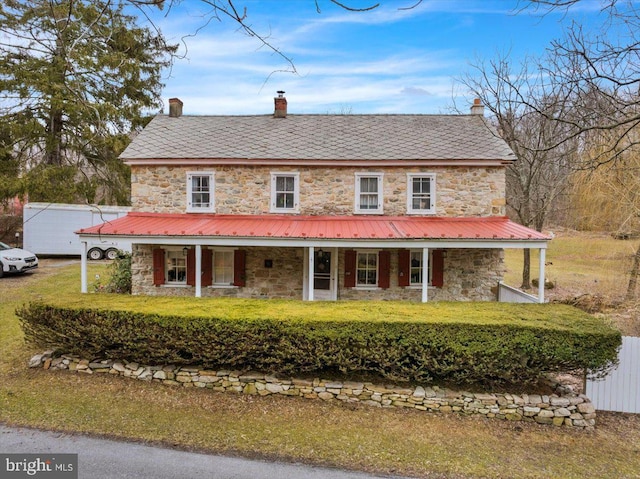 farmhouse inspired home featuring stone siding, covered porch, a chimney, and a high end roof