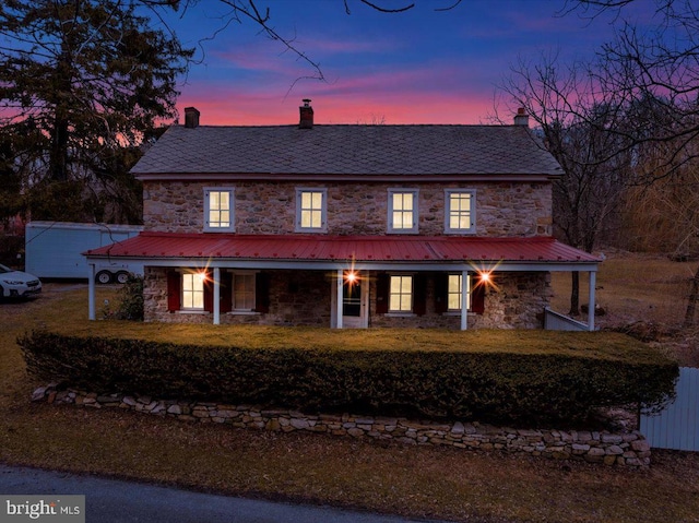 exterior space featuring stone siding, a chimney, a high end roof, and a yard