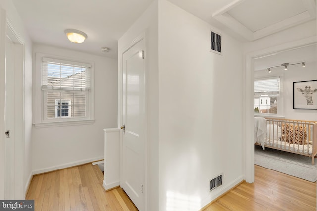 hall featuring light wood-type flooring, a healthy amount of sunlight, and visible vents