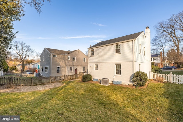 rear view of house with brick siding, a chimney, a lawn, fence private yard, and cooling unit